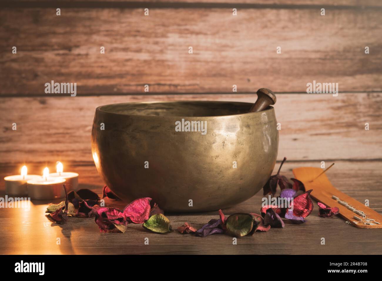 Ciotola tibetana con incenso, candele accese e petali di fiori colorati su un tavolo di legno e spazio copia Foto Stock