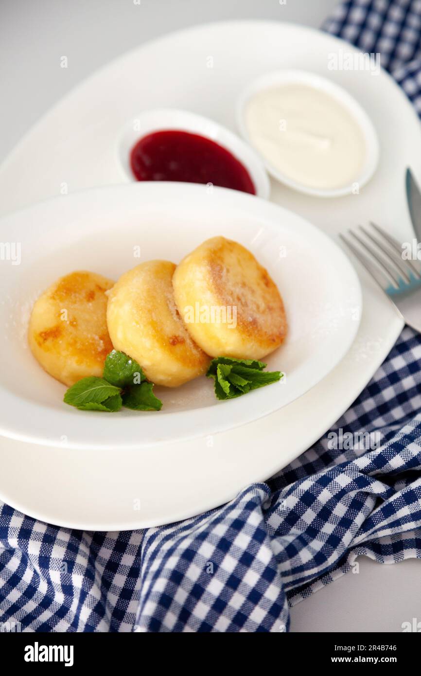 Frittelle di formaggio ricotta rotonda in un piatto bianco su sfondo blu. Cibo prima colazione. Cibo sano. Salsa di panna acida e menta. Primo piano vista dall'alto. Pasto dessert. Frittelle di ricotta al formaggio ricotta. Foto Stock
