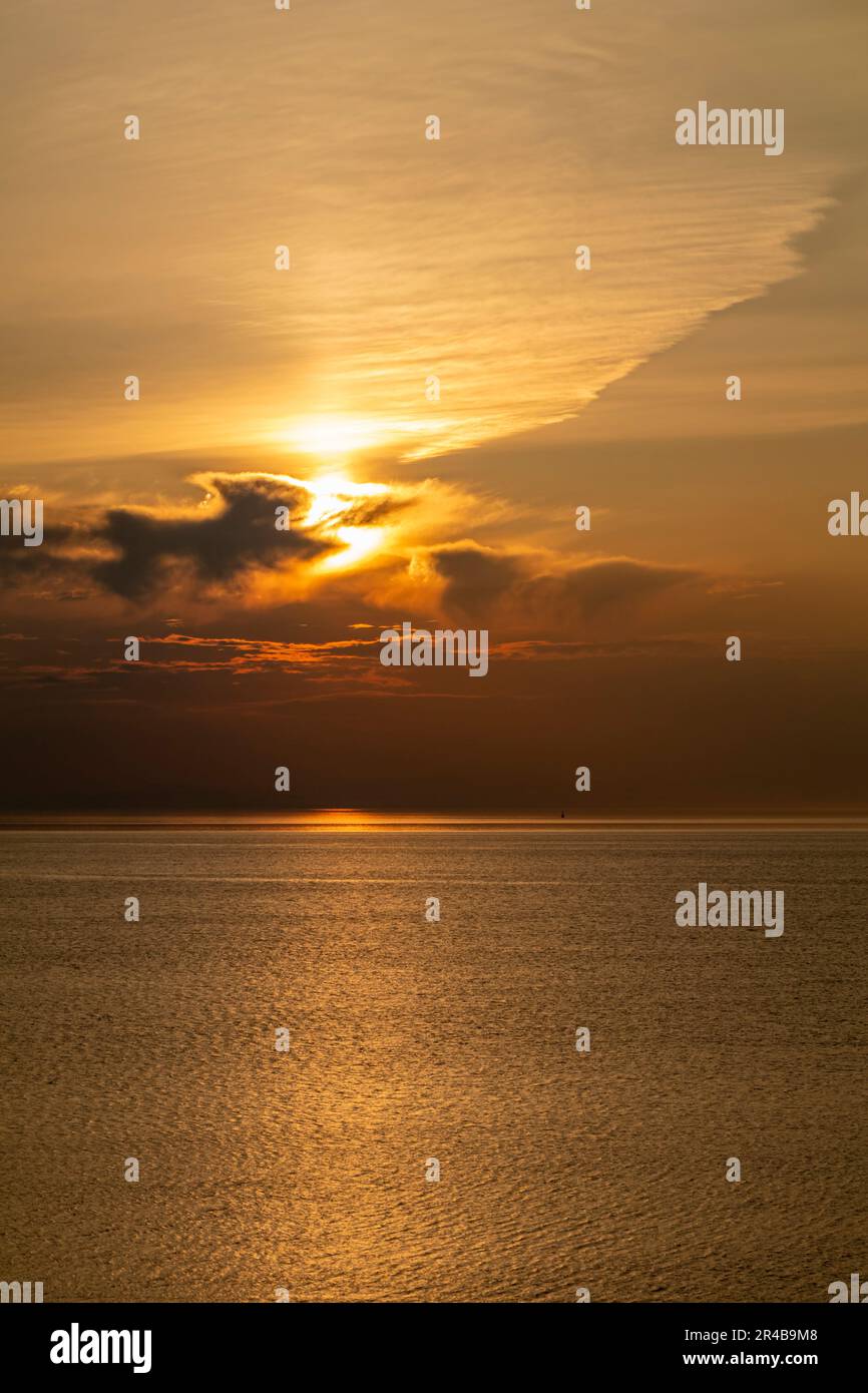 Il tramonto sopra il canale di Bristol come il sole scompare dietro alcune nuvole di copertura all'orizzonte Foto Stock