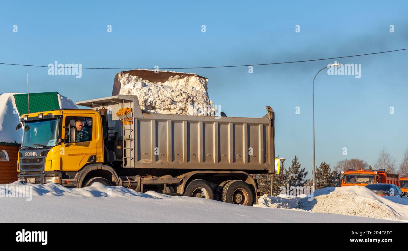Dicembre 23, 2021. Regione di Kemerovo, Russia. Il trattore arancione grande pulisce la neve dalla strada e la carica nel carrello. Pulizia e pulizia della strada Foto Stock