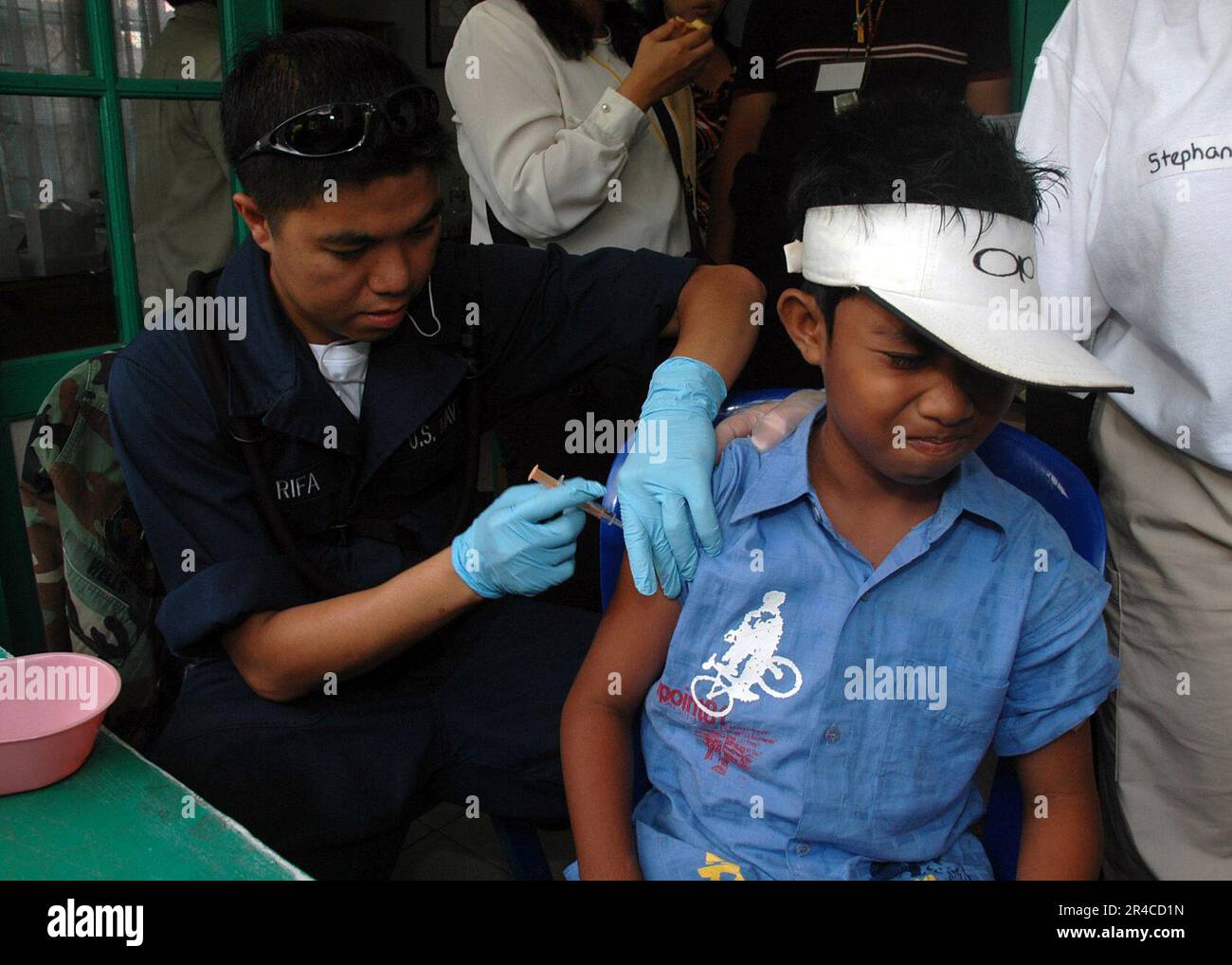 US Navy Navy Hospitalman ha imbarcato con la struttura di trattamento medico a bordo della nave ospedaliera USNS Mercy (T-AH 19) del Military Sealift Command (MSC), amministra un colpo di immunizzazione ad un IC locale. Foto Stock