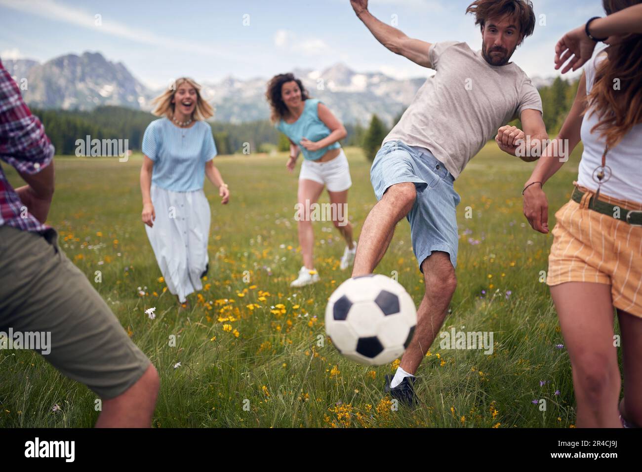 Amici che si divertono all'aperto nella natura. Uomo calci palla di calcio. Divertimento, convivenza, stile di vita, concetto di natura. Foto Stock
