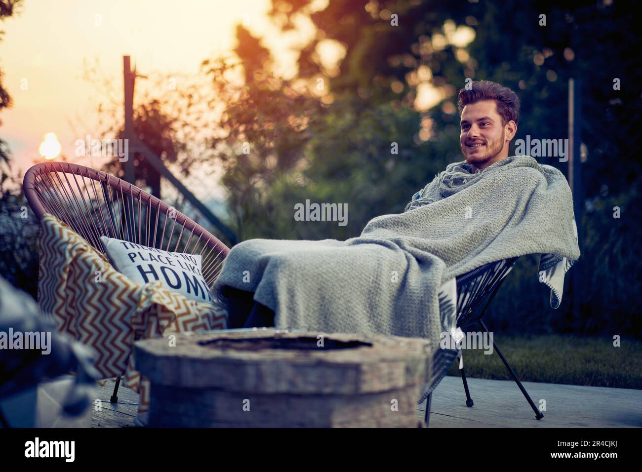 L'uomo si siede nel suo cortile, coperto da una coperta accogliente, e si crogiola nella bellezza di un tramonto. Con un sorriso soddisfatto sul volto, si immerge Foto Stock