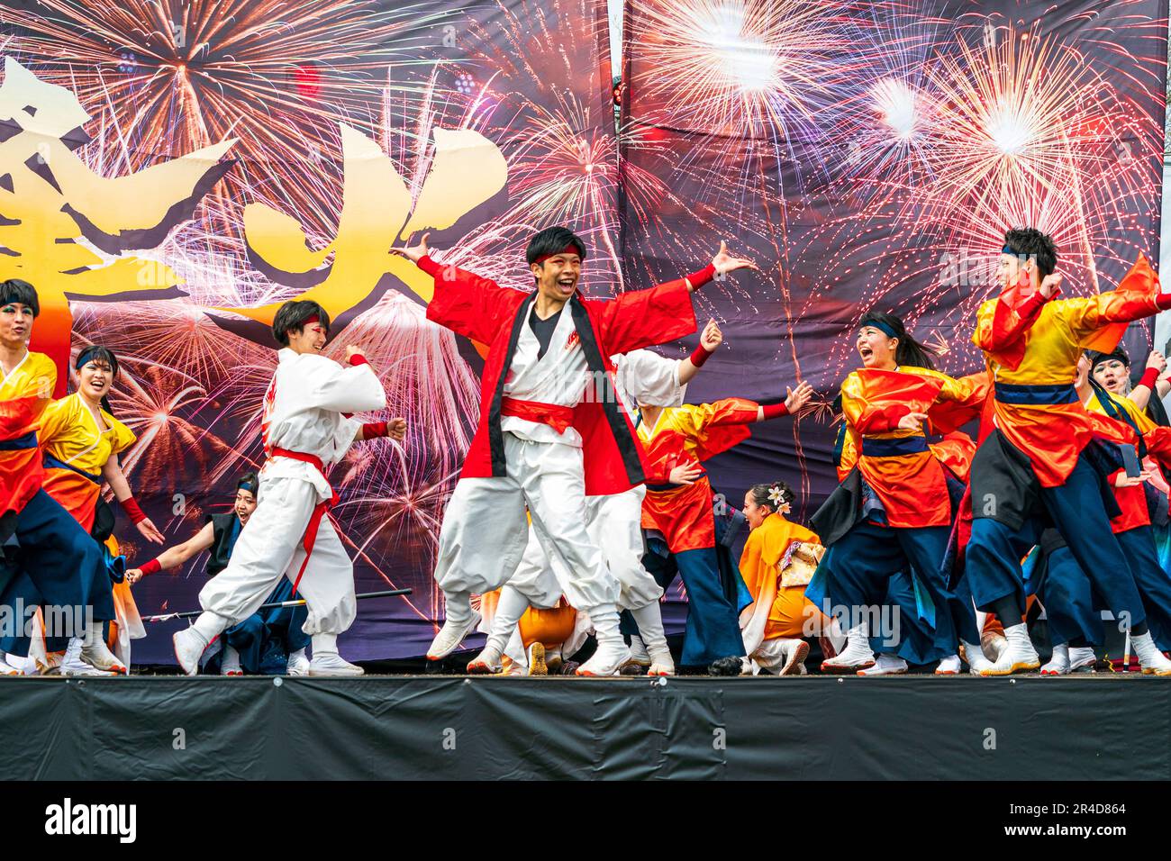 La squadra giapponese di ballerini Yosakoi ballano sul palco davanti a due enormi bandiere che mostrano fuochi d'artificio al festival Kyusyu Gassai, Kumamoto. Foto Stock