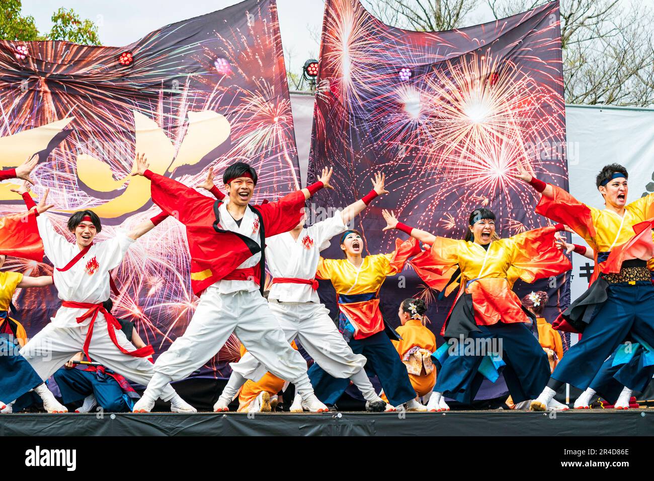La squadra giapponese di ballerini Yosakoi ballano sul palco davanti a due enormi bandiere che mostrano fuochi d'artificio al festival Kyusyu Gassai, Kumamoto. Foto Stock