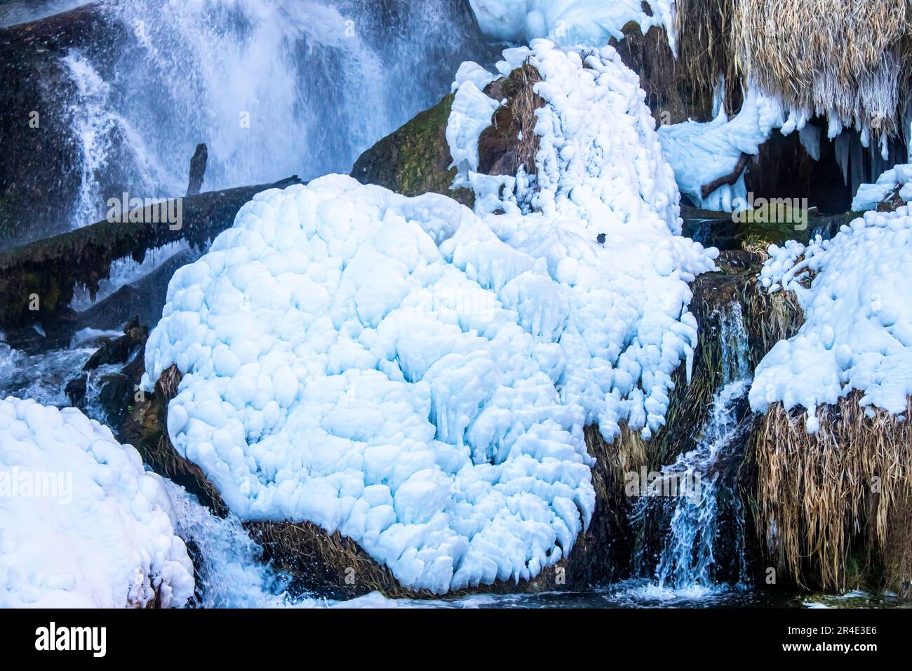 Una maestosa cascata ghiacciata che scende lungo una parete cristallina della scogliera, circondata da splendide formazioni ghiacciate Foto Stock