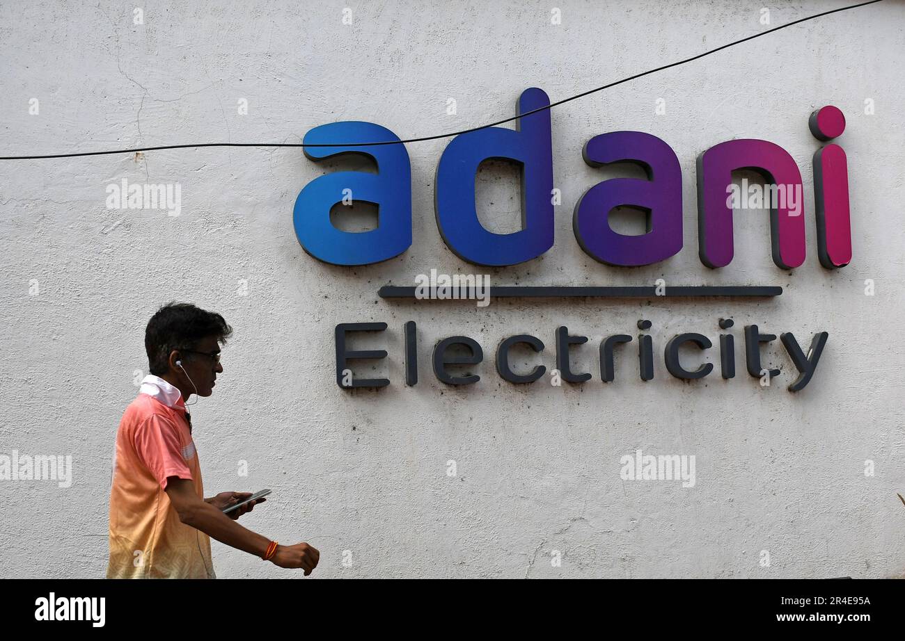 Un uomo in possesso di un telefono cellulare passa davanti al logo dell'elettricità Adani sul muro di Mumbai. Adani Power and Energy è una delle più grandi società di distribuzione di energia in India, che fa parte del gruppo di società Adani. Foto Stock