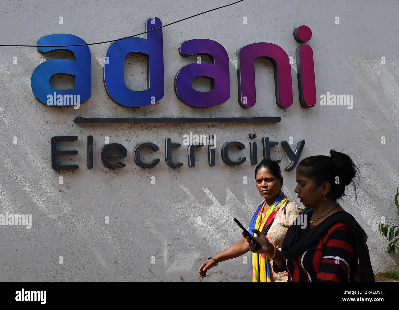 Mumbai, India. 27th maggio, 2023. Le donne passano davanti al logo dell'elettricità Adani sulla parete di Mumbai. Adani Power and Energy è una delle più grandi società di distribuzione di energia in India, che fa parte del gruppo di società Adani. (Foto di Ashish Vaishnav/SOPA Images/Sipa USA) Credit: Sipa USA/Alamy Live News Foto Stock