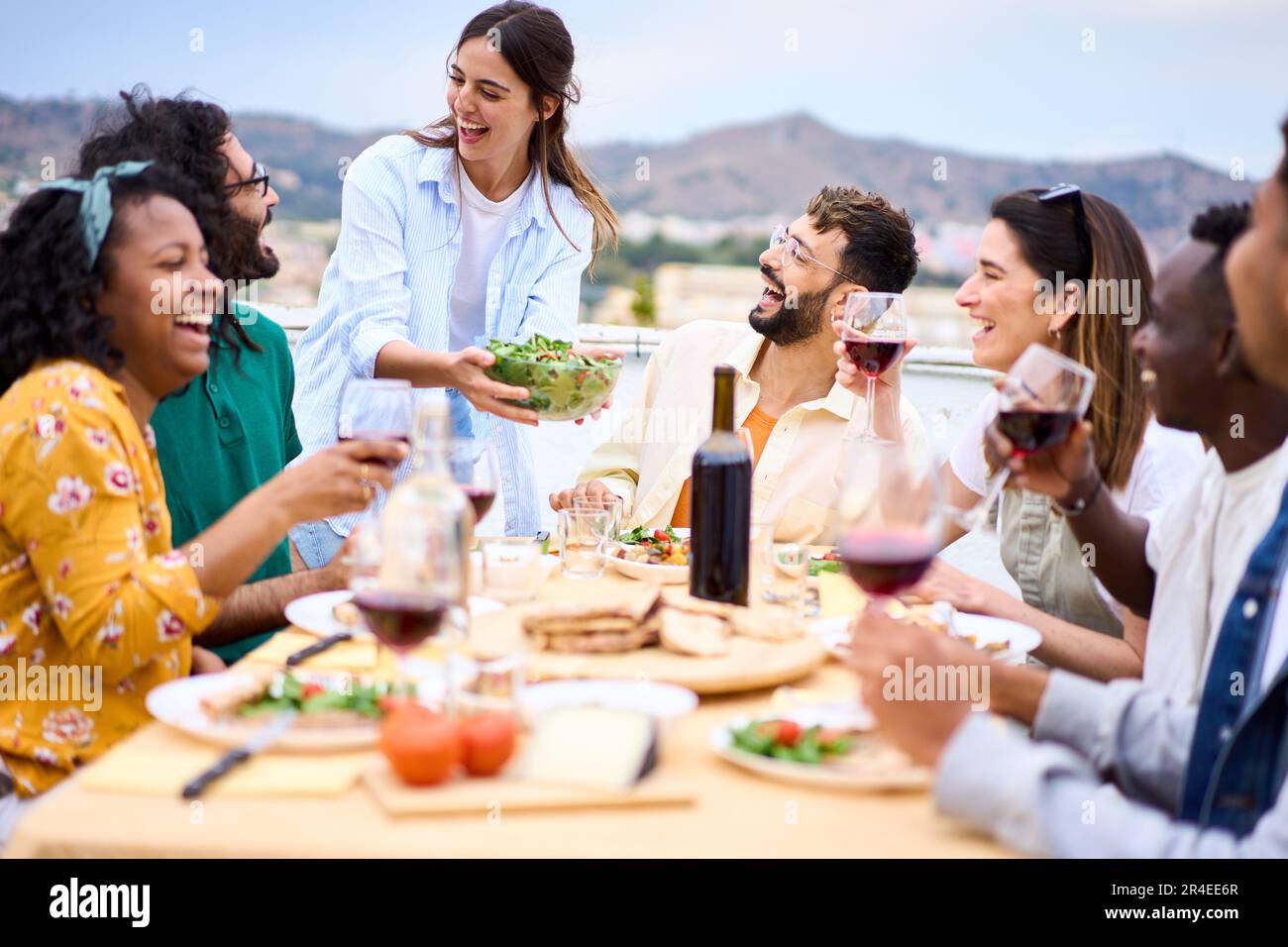 Giovane donna caucasica sorridente mettendo piatto cibo sul tavolo a celebrazione felici amici sul tetto. Foto Stock