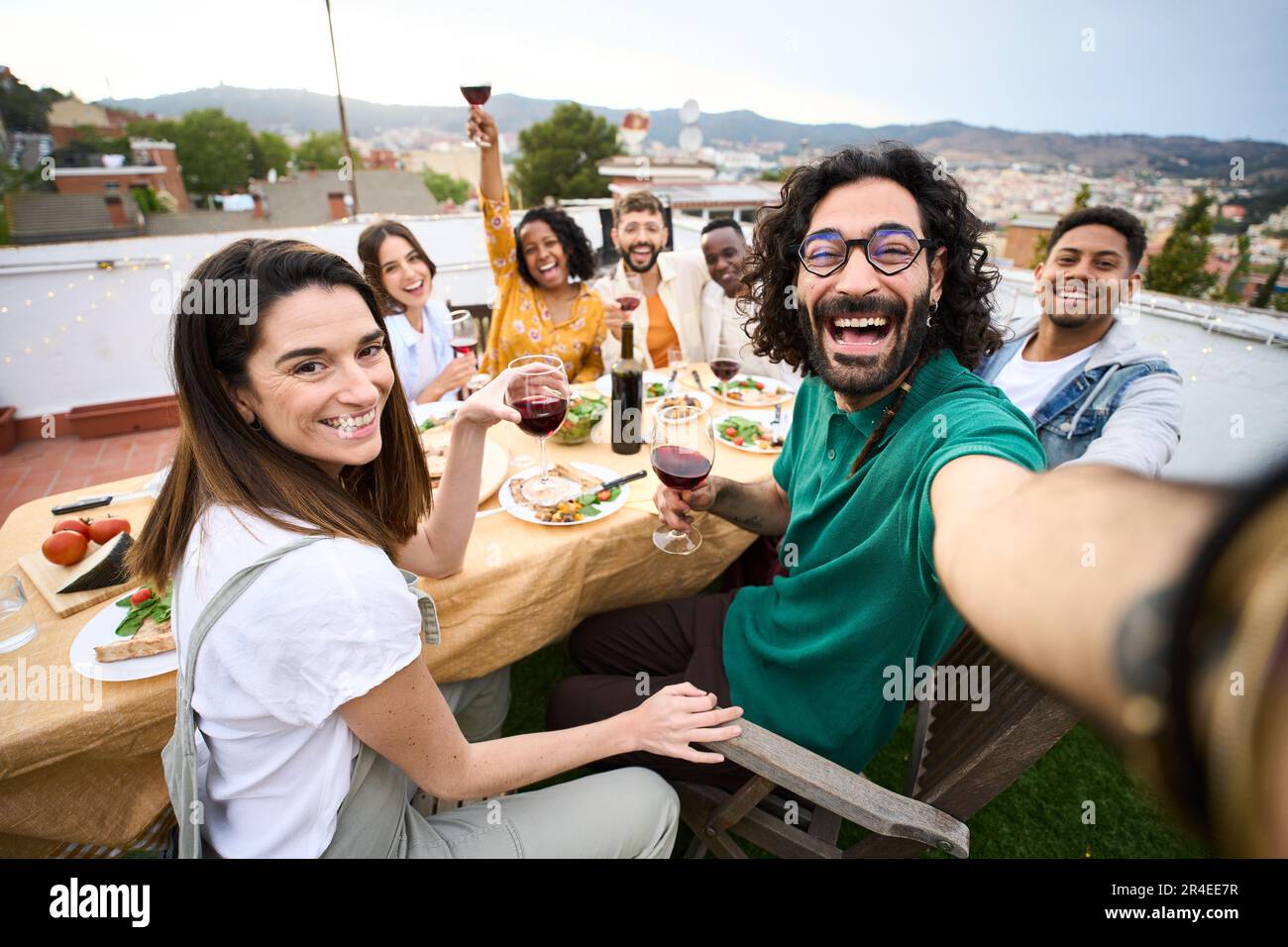 Gruppo di amici multirazziali che si divertono al party sul tetto. Uomo che prende selfie alla gente al barbecue. Foto Stock