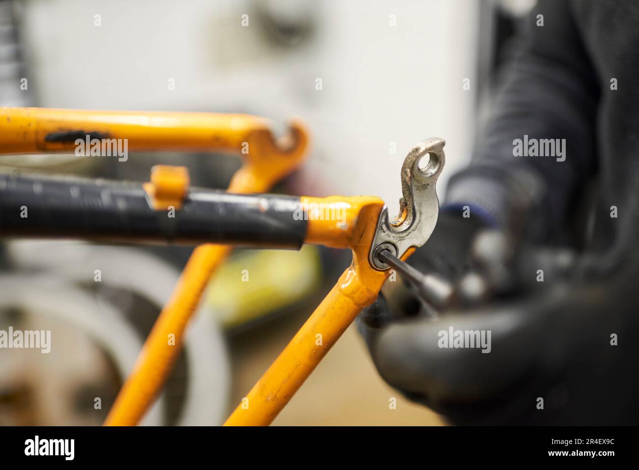 Riparazione di una bicicletta: Mani di una persona irriconoscibile utilizzando guanti smontando una bicicletta arancione nella sua officina. Composizione selettiva della messa a fuoco. Foto Stock