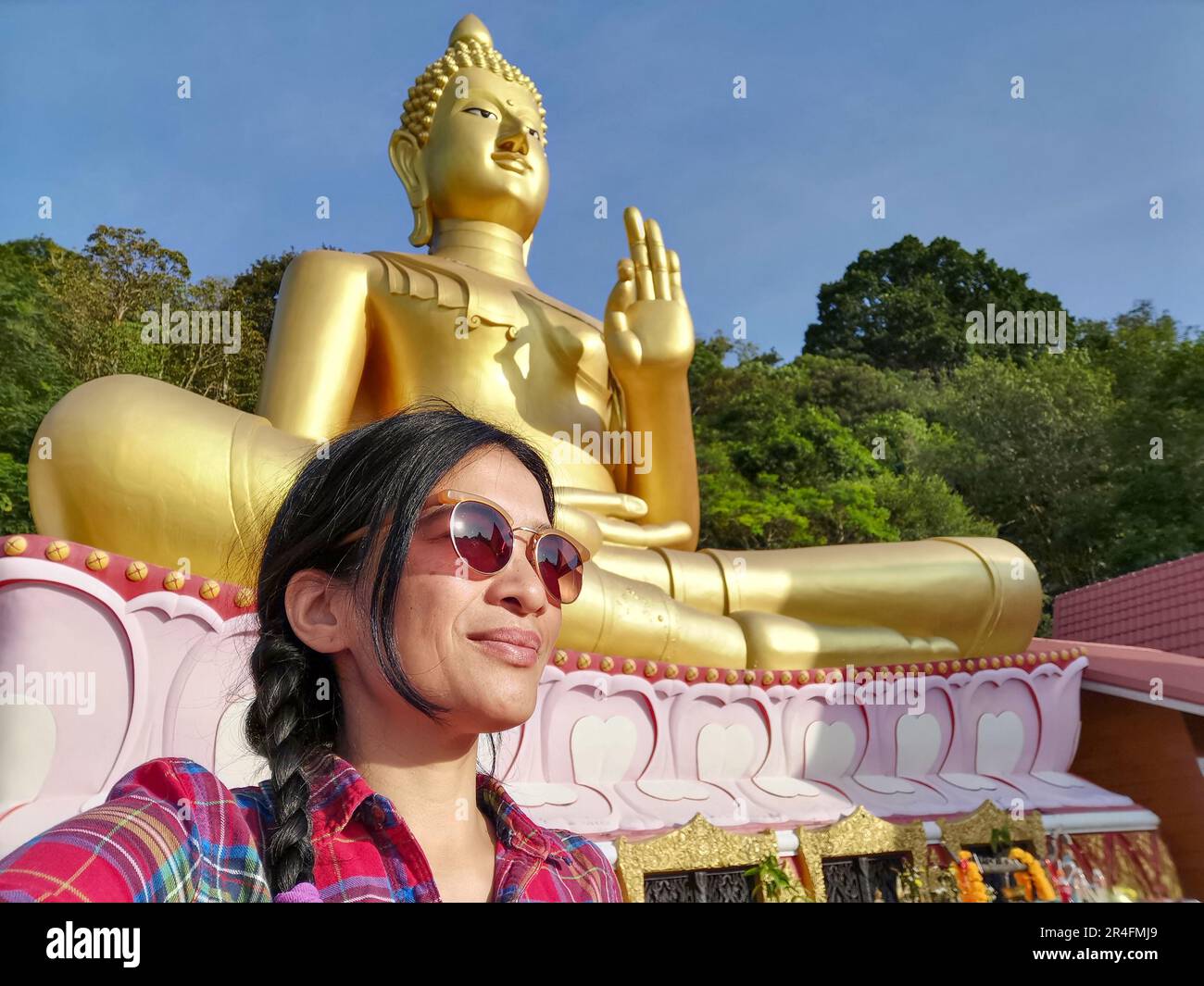Una giovane donna tailandese che prende un selfie di fronte a una statua del Buddha a Wat Khao Rang, un tempio buddista a Phuket, Thailandia. Foto Stock
