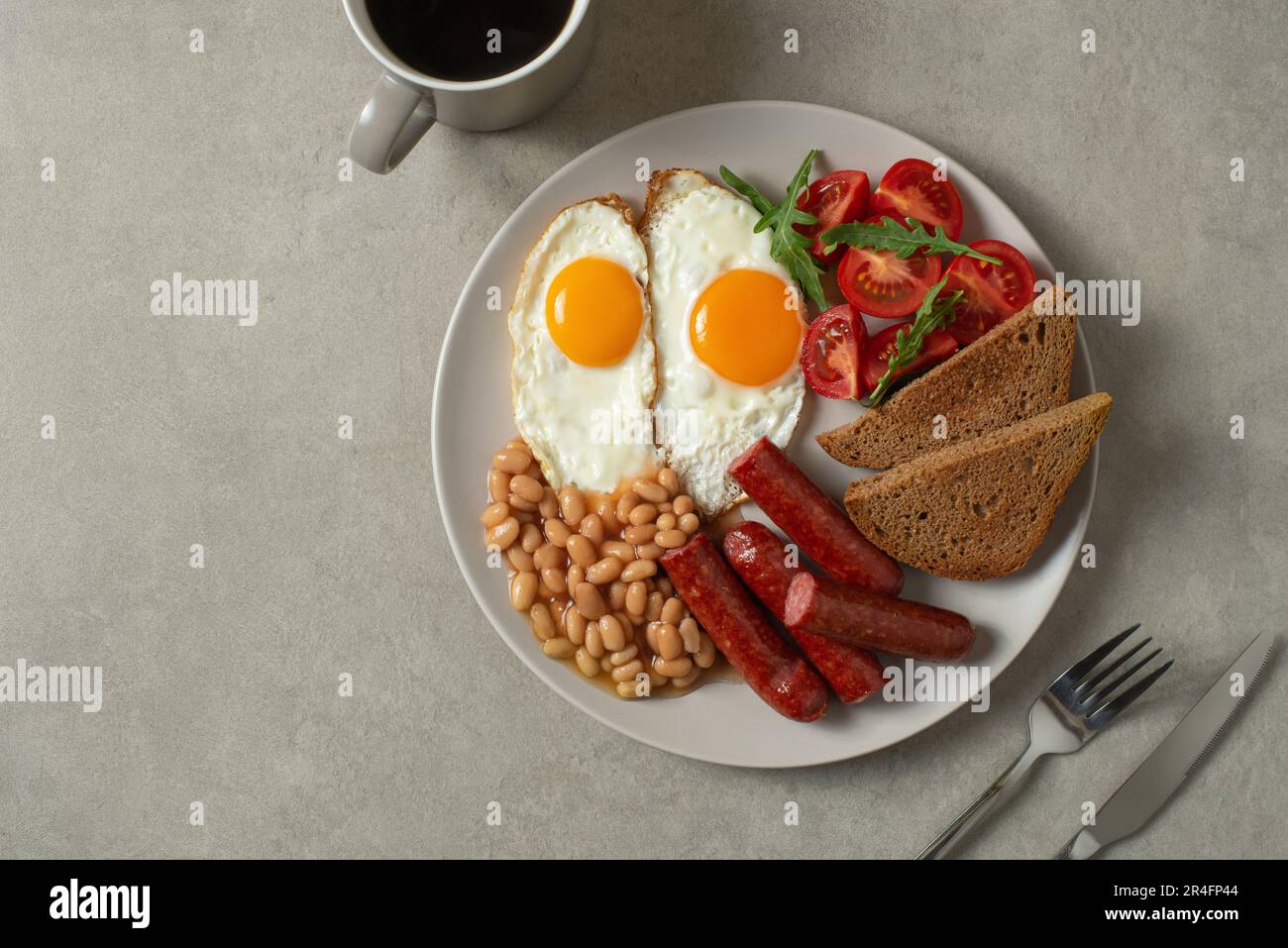 Uova fritte con salsicce e fagioli in un piatto su sfondo grigio. Colazione all'inglese Foto Stock