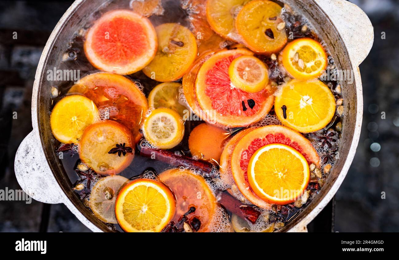 Vite speziata tritata con arance in vaso nel mercato alimentare di strada. Bevanda alcolica calda colorata al closeup del festival della fiera all'aperto Foto Stock