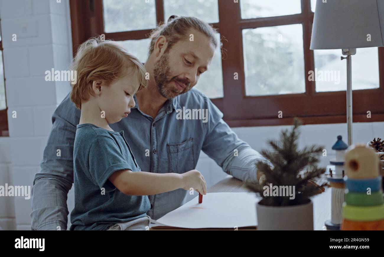 Famiglia caucasica pittura su carta con figlio in casa. Little Son imparare a disegnare l'immagine d'arte Godetevi la creatività con il padre in casa. Foto Stock