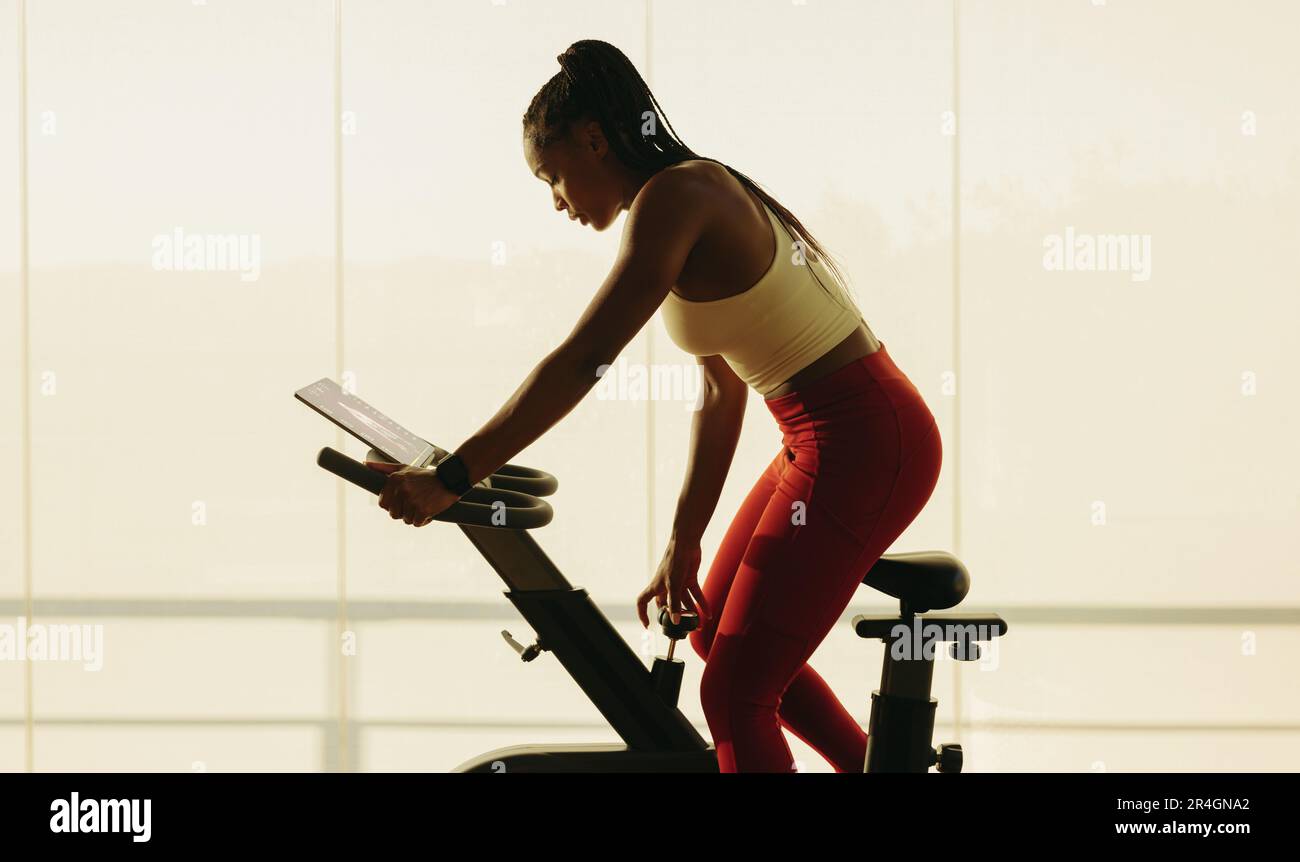 Donna nera che si spinge a nuove altezze nel suo viaggio di fitness, partecipando a una impegnativa lezione di ciclismo virtuale. Donna schiacciare il suo fitness andare Foto Stock