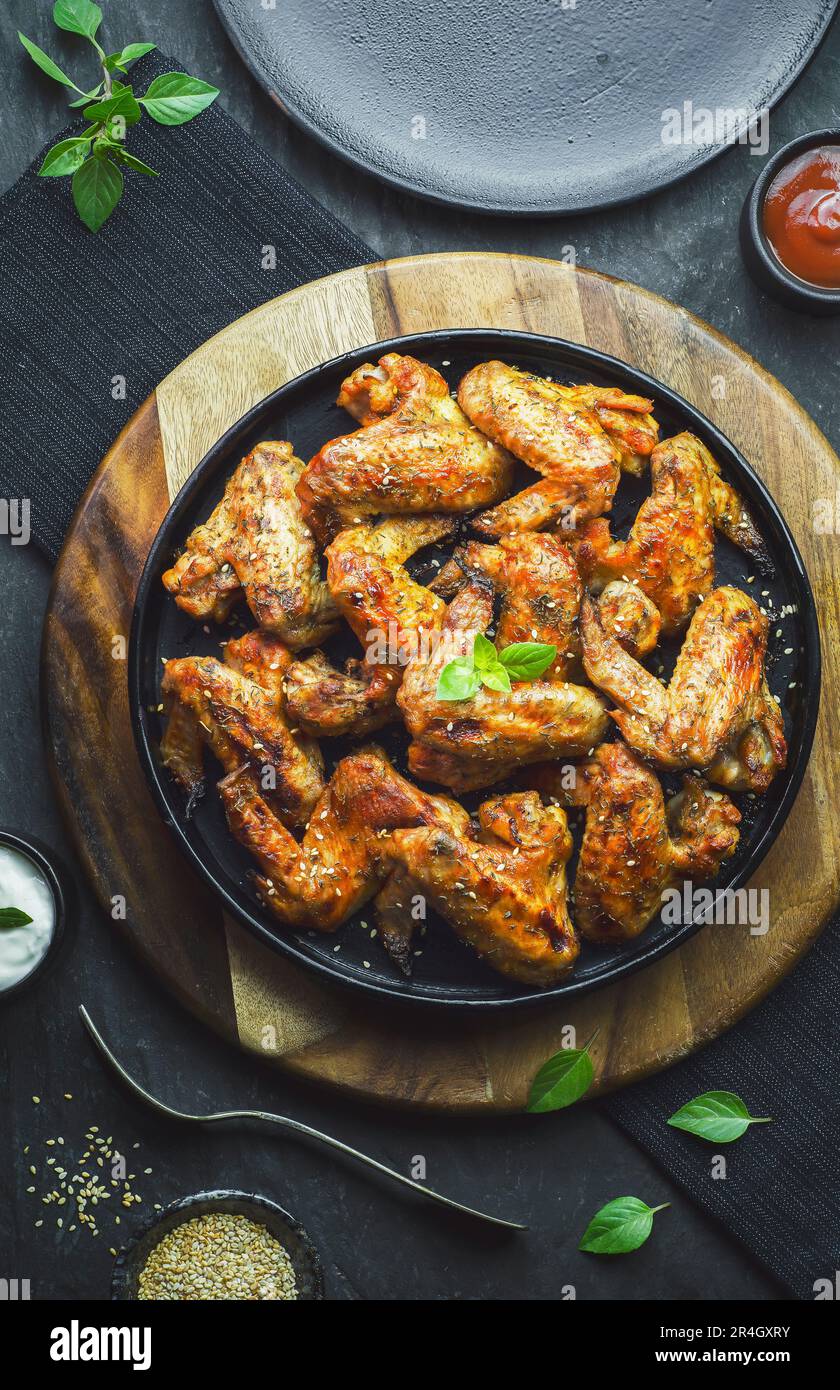 Deliziose ali di pollo con sesamo e gustose salse su sfondo scuro. Vista dall'alto con primo piano. Foto Stock