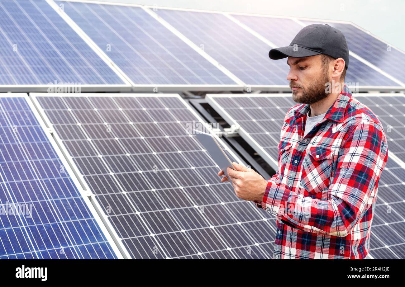 Titolo: Supervisore tecnico sul campo che utilizza un tablet digitale per la valutazione delle prestazioni dei pannelli solari nella fattoria di energia solare. Foto Stock