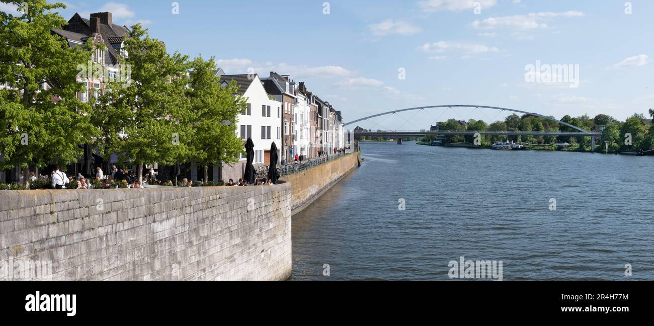 Muro di banchina con persone sedute sulla terrazza lungo il fiume Maas nel quartiere 'Wyck' nella città olandese di Maastricht con il 'Hoge Brug' Foto Stock