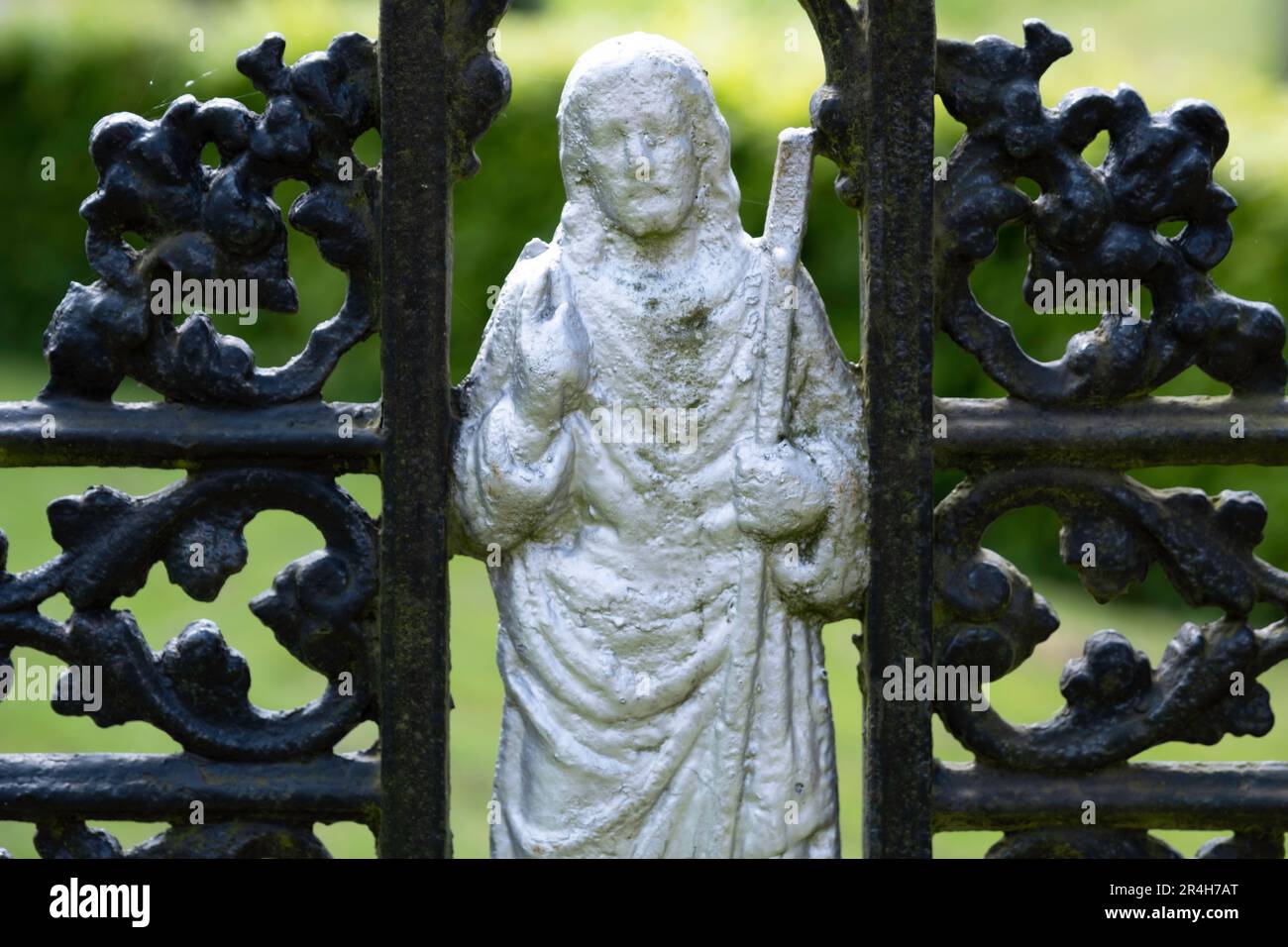 Particolare di una figura di Gesù Cristo con un libro e un bastone in mano tra una croce di metallo decorata dipinta di nero, vicino ad una lapide in un cimitero Foto Stock