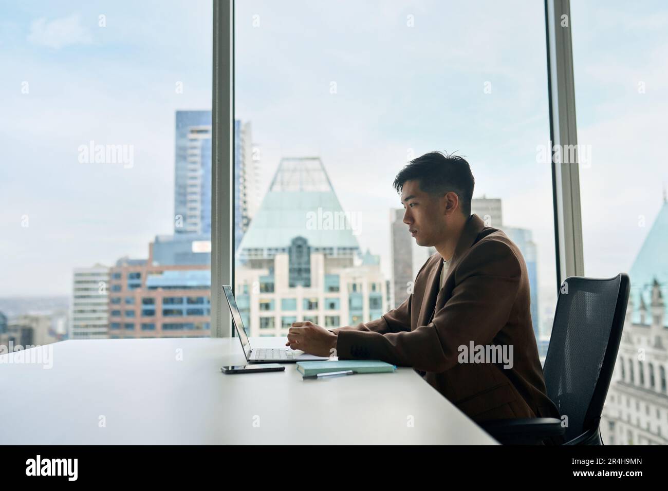 Giovane uomo d'affari asiatico che lavora al computer portatile in ufficio. Foto Stock