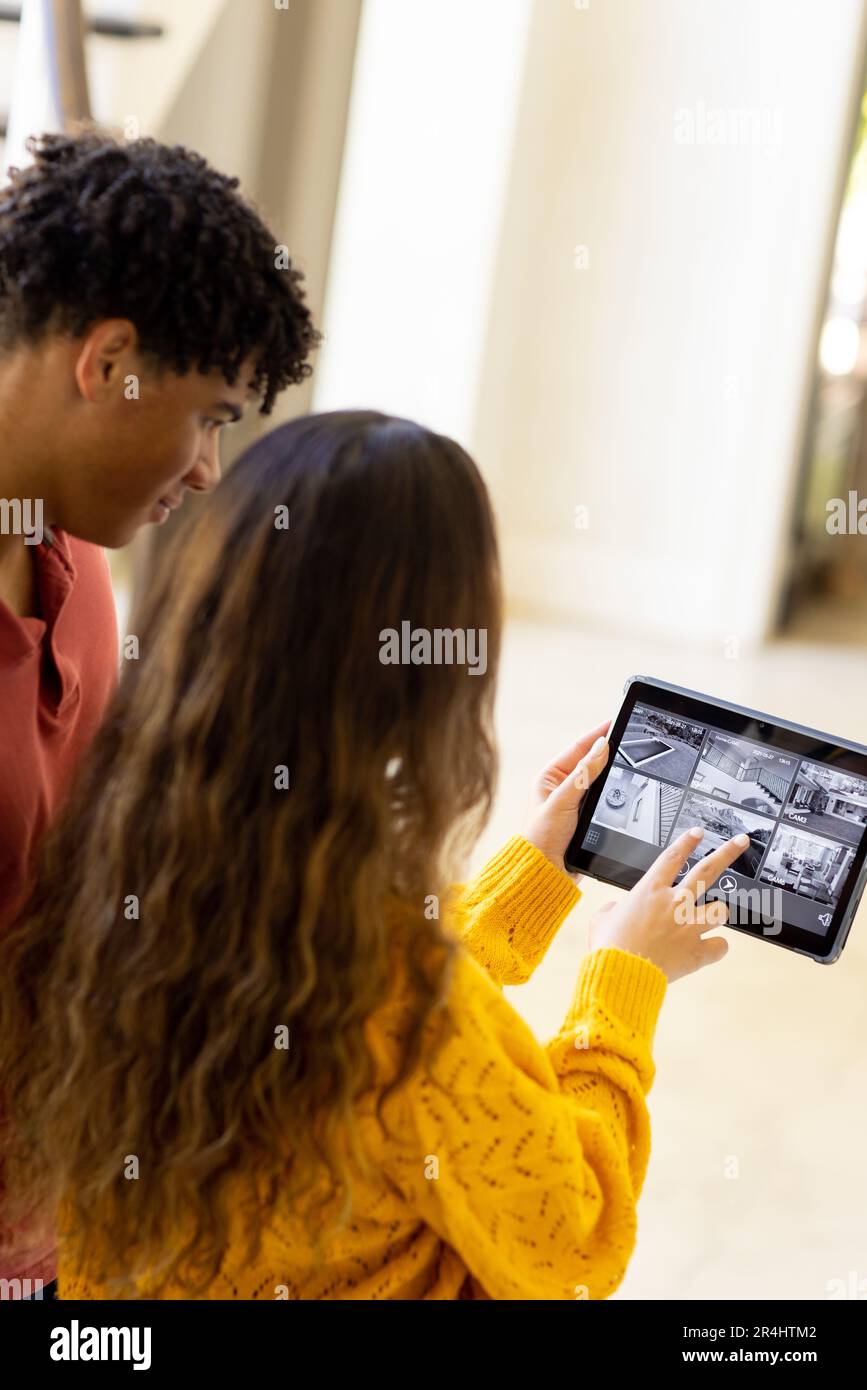 Giovane coppia biraciale che controlla la casa con videocamera su tablet digitale Foto Stock