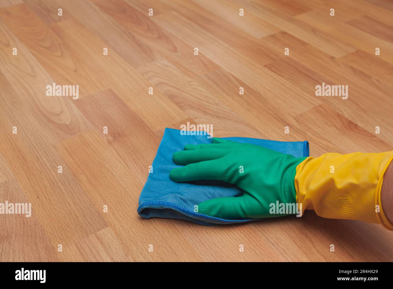 La mano di una persona irriconoscibile che indossa un guanto di gomma che pulisce il pavimento in parquet con un panno in microfibra blu. Foto Stock
