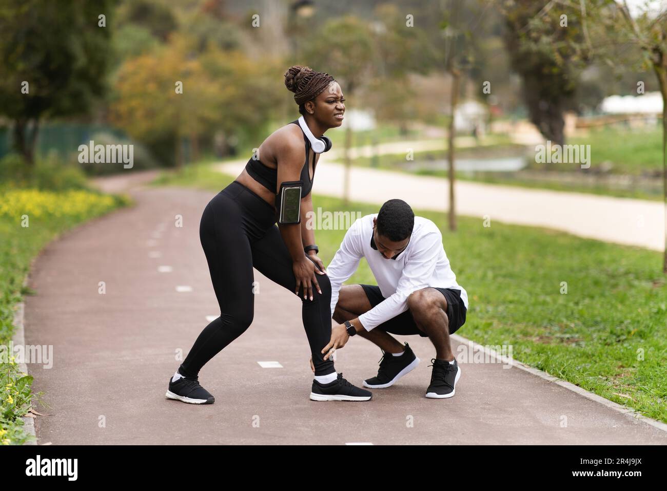 Giovane uomo nero in abbigliamento sportivo aiuta a donna su strada, che  soffre di lesioni alle gambe nel parco estivo Foto stock - Alamy