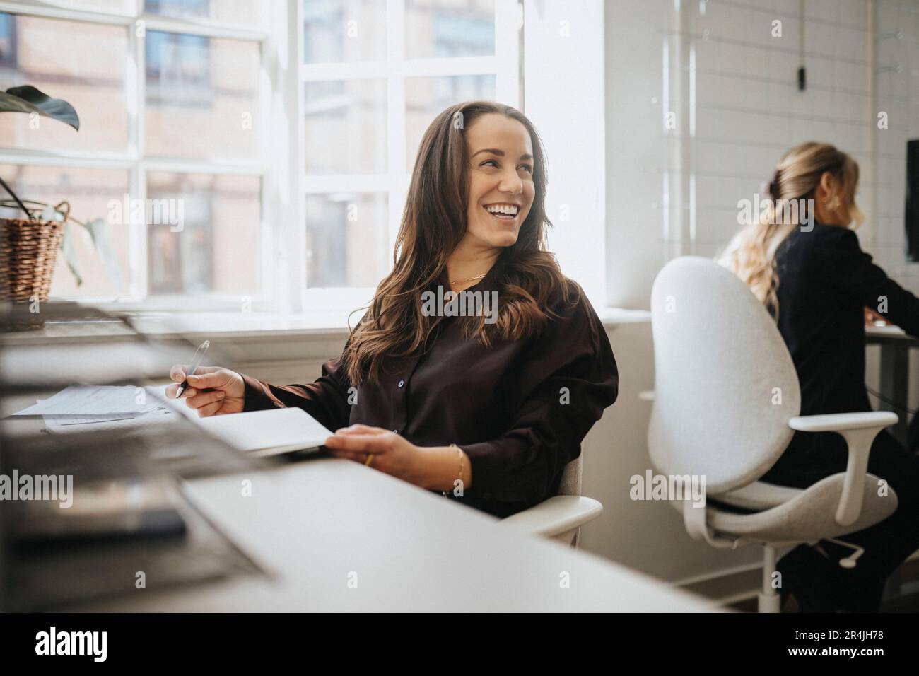 Felice imprenditore donna che guarda lontano mentre seduto alla scrivania in ufficio Foto Stock