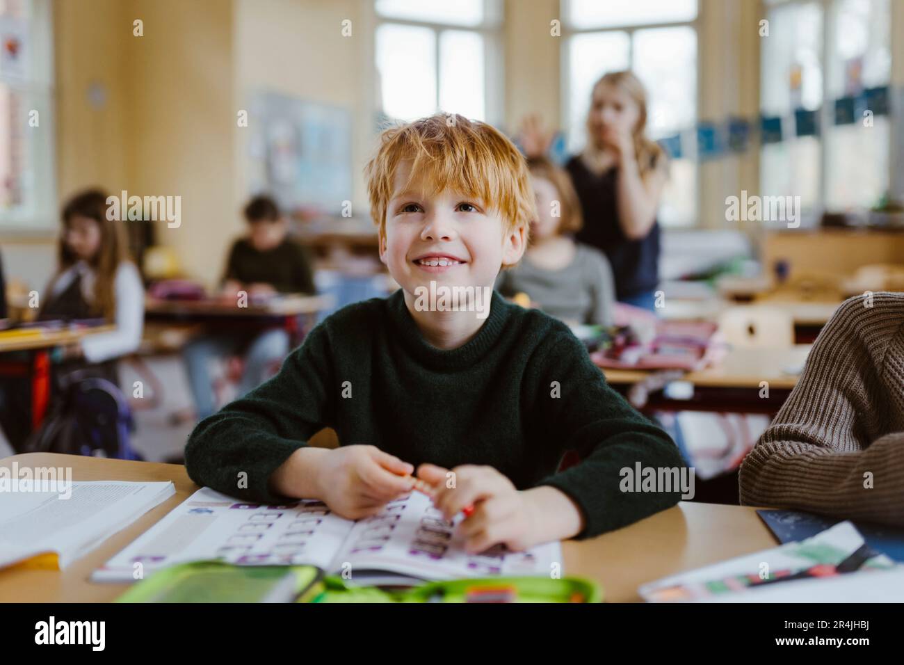 Pupilla sorridente con capelli biondi seduti alla scrivania in classe Foto Stock