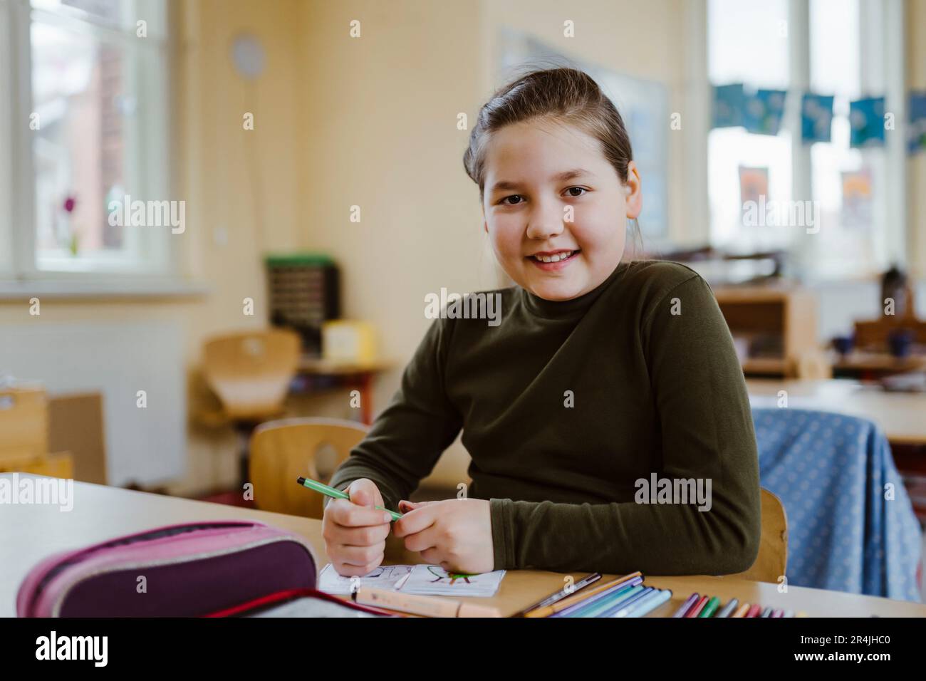 Ritratto di una pupilla sorridente seduta alla scrivania in aula Foto Stock