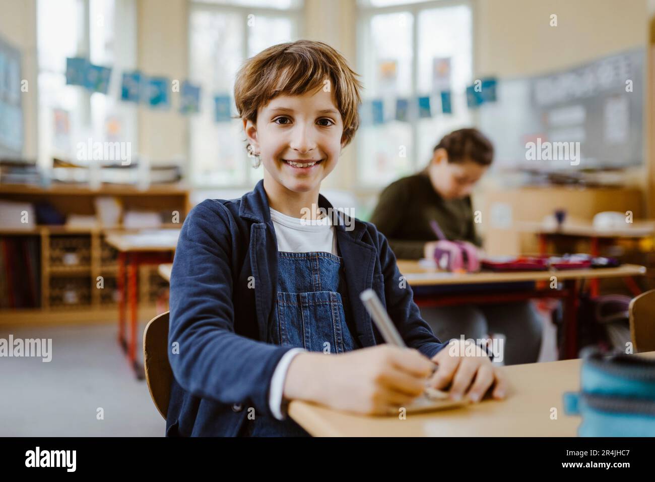 Ritratto di un ragazzo sorridente seduto alla scrivania in classe Foto Stock