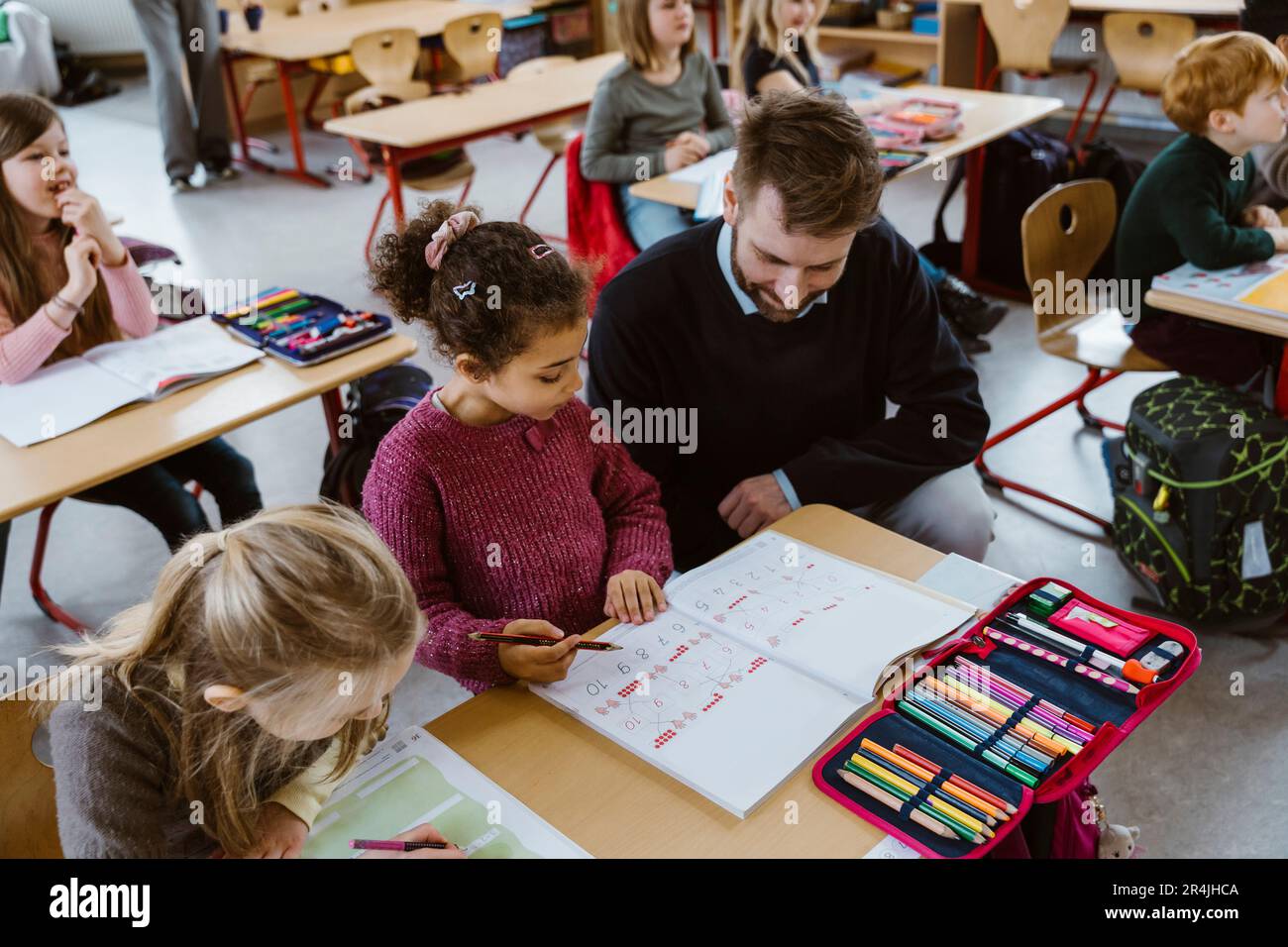 Vista ad alto angolo dell'insegnante maschile accovacciato dalla scolastica che risolve la matematica in classe Foto Stock