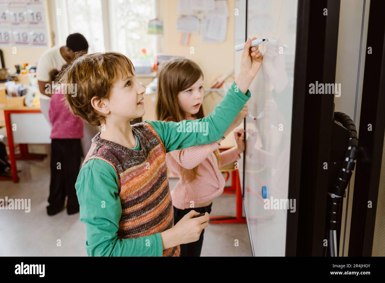 Ragazzo scrivere sulla lavagna mentre risolvere il problema di matematica da ragazza in classe Foto Stock