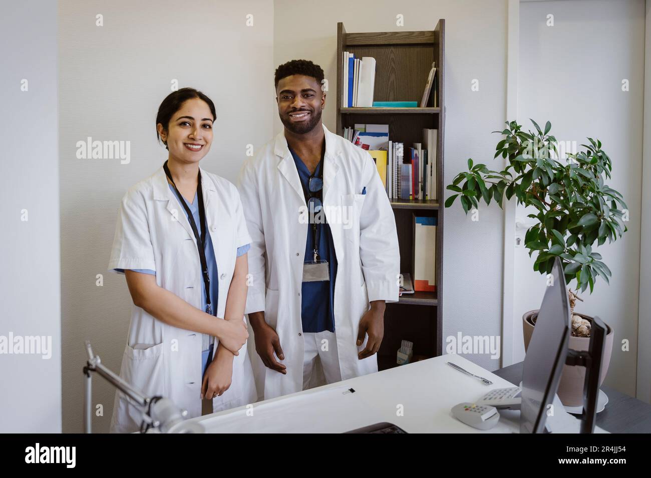 Ritratto di operatori sanitari sicuri di sesso maschile e femminile in piedi alla scrivania presso la clinica Foto Stock
