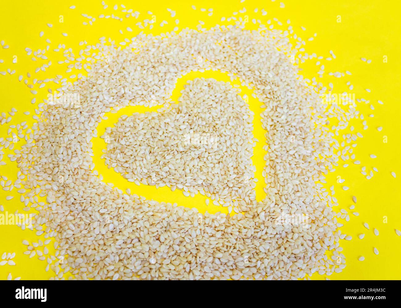 Cuore fatto di semi di Sesamo su uno sfondo giallo. Semi di sesamo su un primo piano di sfondo giallo. Foto Stock