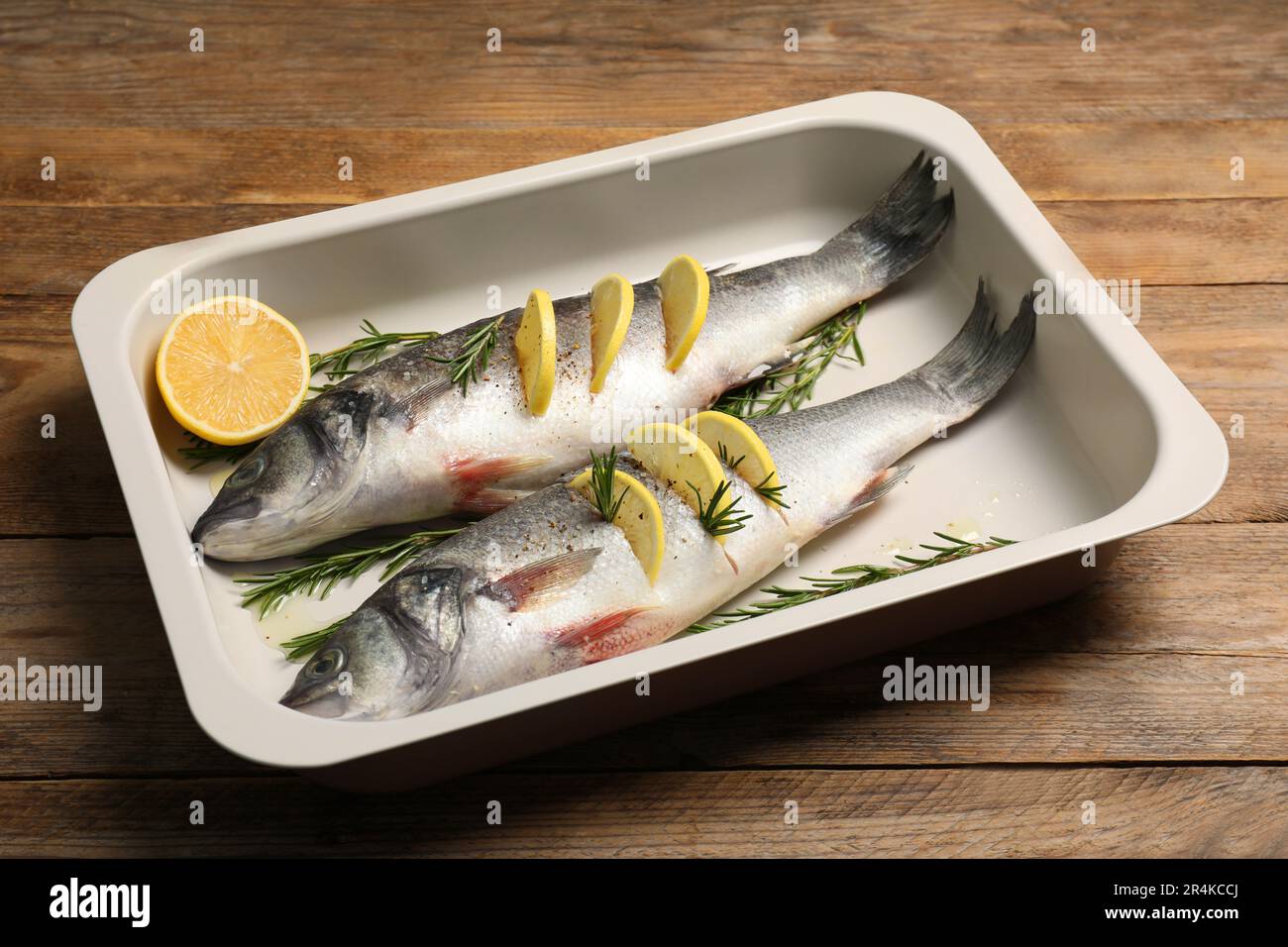 Vassoio da forno con pesce branzino crudo, limone e rosmarino su tavola di legno Foto Stock