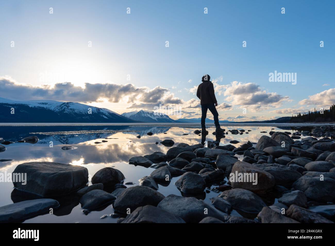 Turisti che si trovano accanto all'enorme lago di Atlin, British Columbia durante la primavera tramonto riflessione rocce lago. Foto Stock