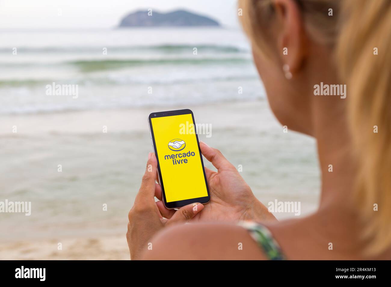 Applicazione Mercado Livre sullo schermo dello smartphone. Donna in spiaggia che ha un telefono con un'applicazione per il mercato online. E-commerce, marchio latino-americano. Foto Stock