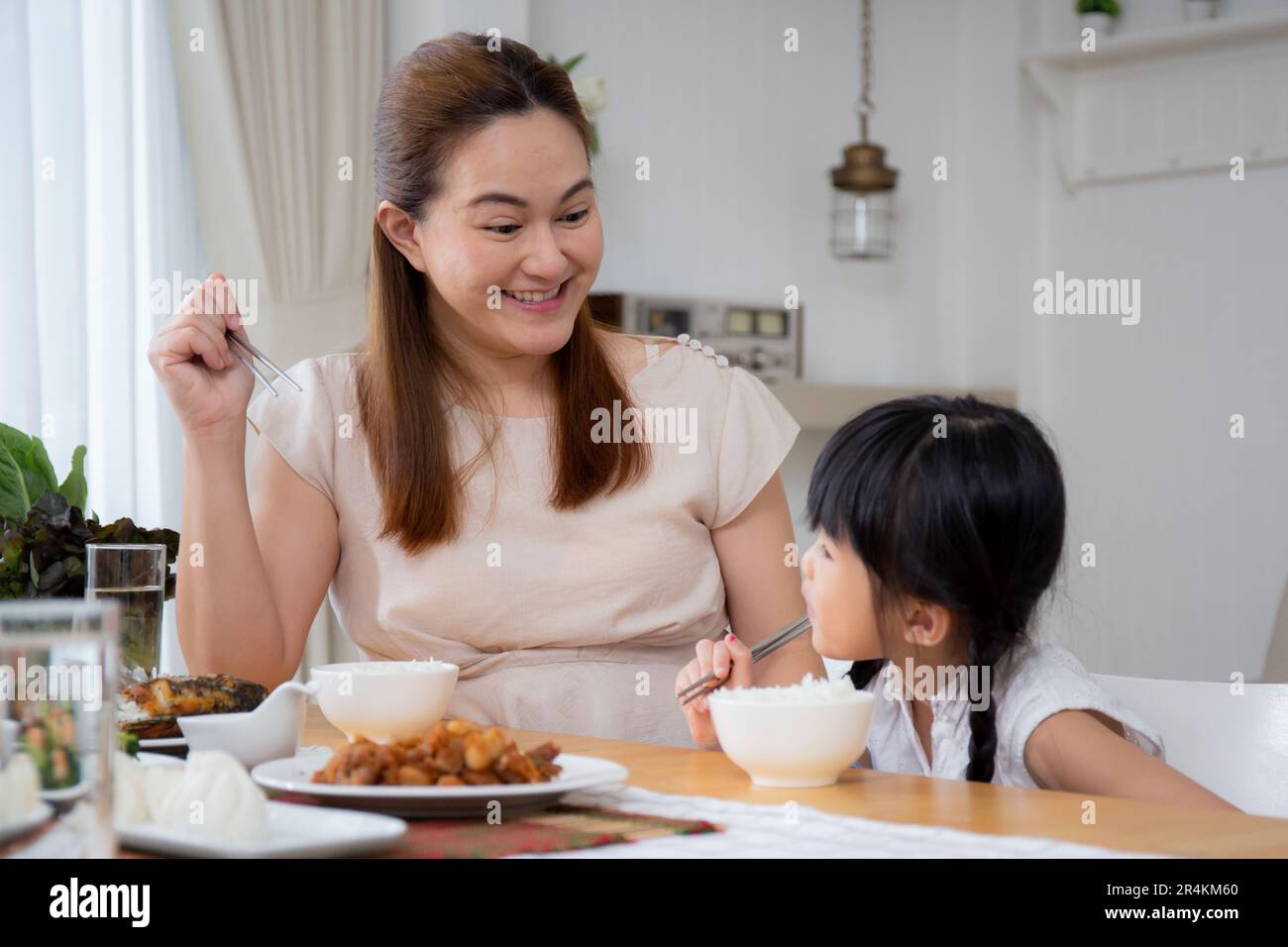 Felicità famiglia asiatica madre e figlia mangiare cibo in cucina insieme a casa, genitori e bambini seduti a pranzo in soggiorno, legame e relazione Foto Stock