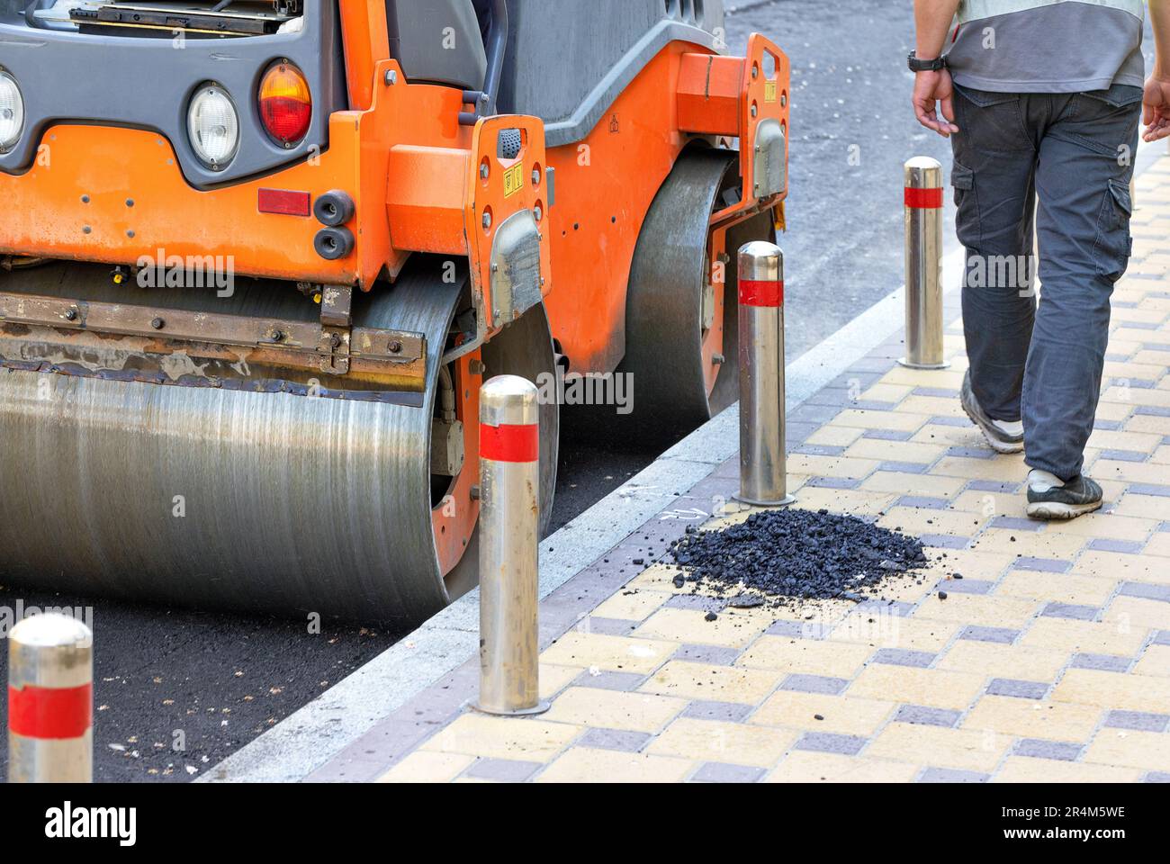 Il rullo vibrante stradale con le sue ruote in metallo compatta l'asfalto fresco con alta precisione lungo il bordo della strada lungo il marciapiede pavimentato. Foto Stock
