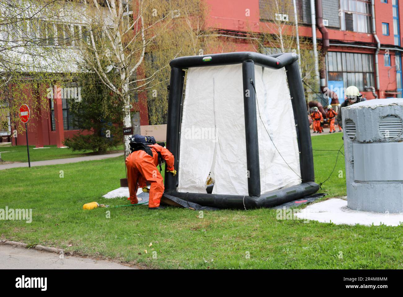 Un pompiere professionale in una speciale tuta ignifuga arancione si prepara ad assemblare una tenda ad ossigeno bianco per salvare le persone in una raffineria chimica, petrolifera, Foto Stock
