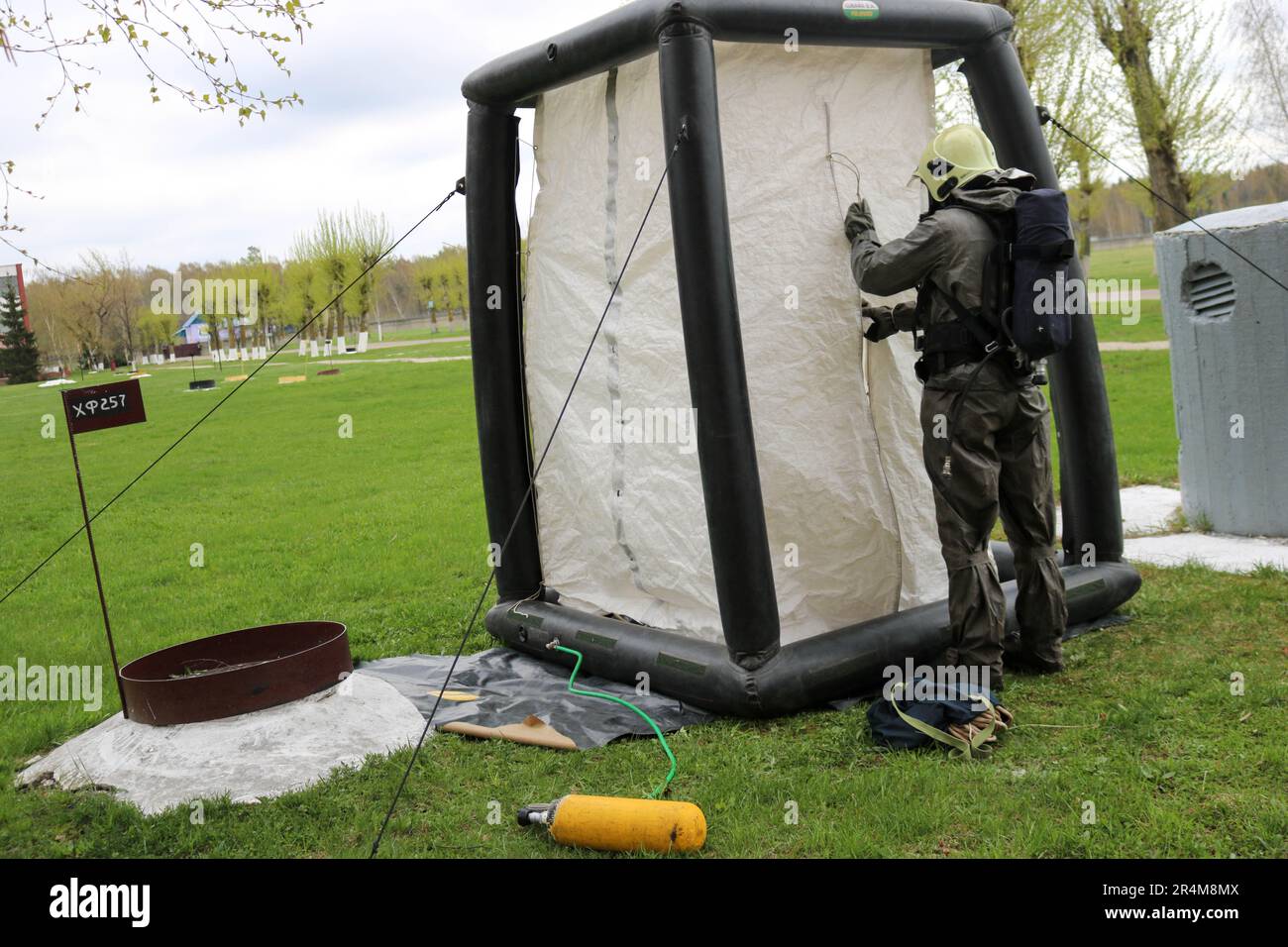 Un pompiere professionale in una speciale tuta nera ignifuga si prepara ad assemblare una tenda di ossigeno bianca per salvare le persone in una raffineria chimica, in pe Foto Stock
