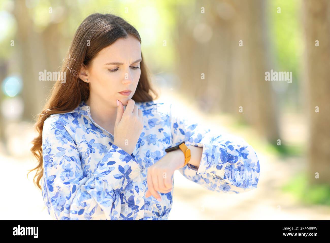 Donna preoccupata che controlla lo smartwatch camminando in un parco Foto Stock