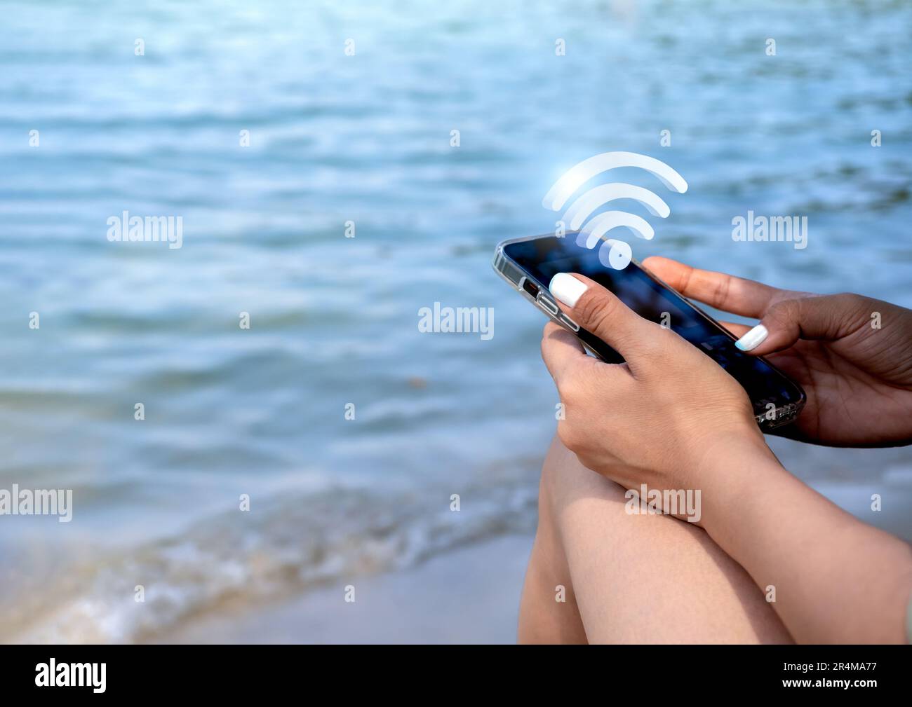 Wi-Fi, icona 3D virtuale su smartphone. Il simbolo della condivisione Wi-fi appare sul cellulare tenuto da un'elegante donna in spiaggia con il mare e la sabbia sul dorso Foto Stock