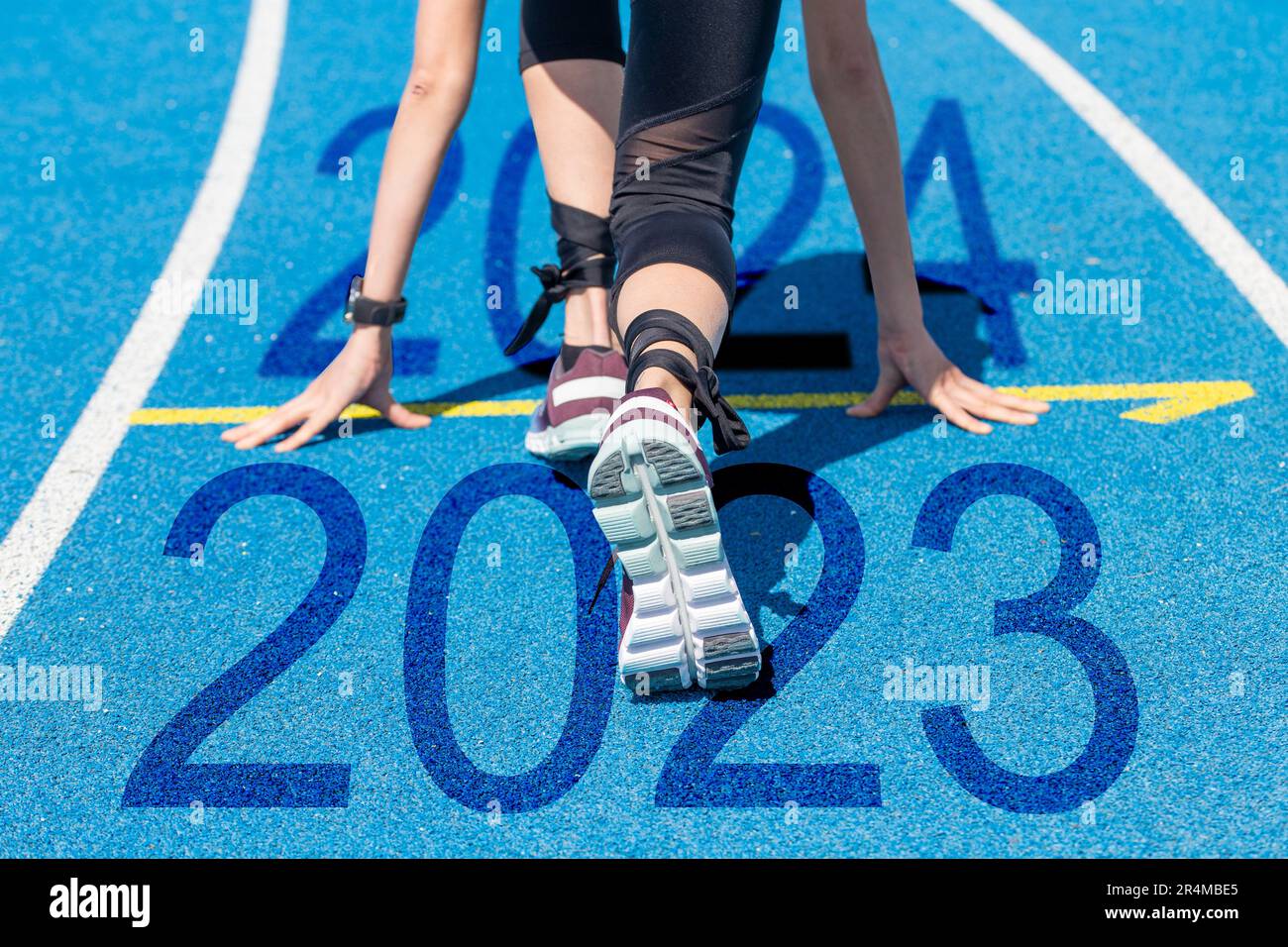 I saluti di Capodanno 2024: Atleta di pista e campo all'inizio, gli anni 2023 e 2024 sono scritti sulla pista tartan Foto Stock