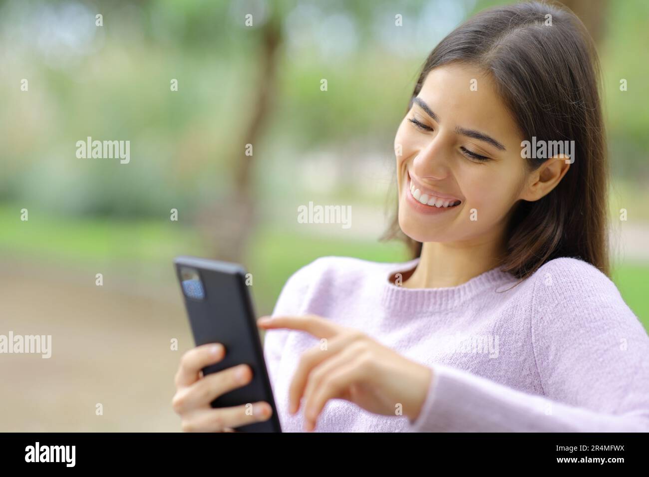 Donna felice sta usando il telefono delle cellule che siede in un parco Foto Stock