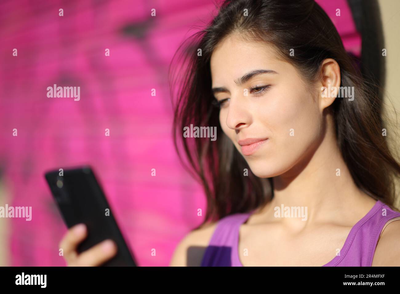Bella donna che controlla il telefono appoggiato in una parete viola Foto Stock