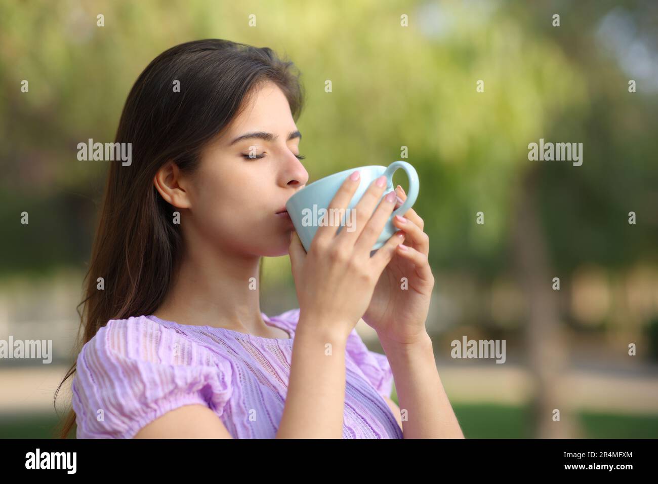 Donna che beve caffè in piedi in un parco da solo Foto Stock
