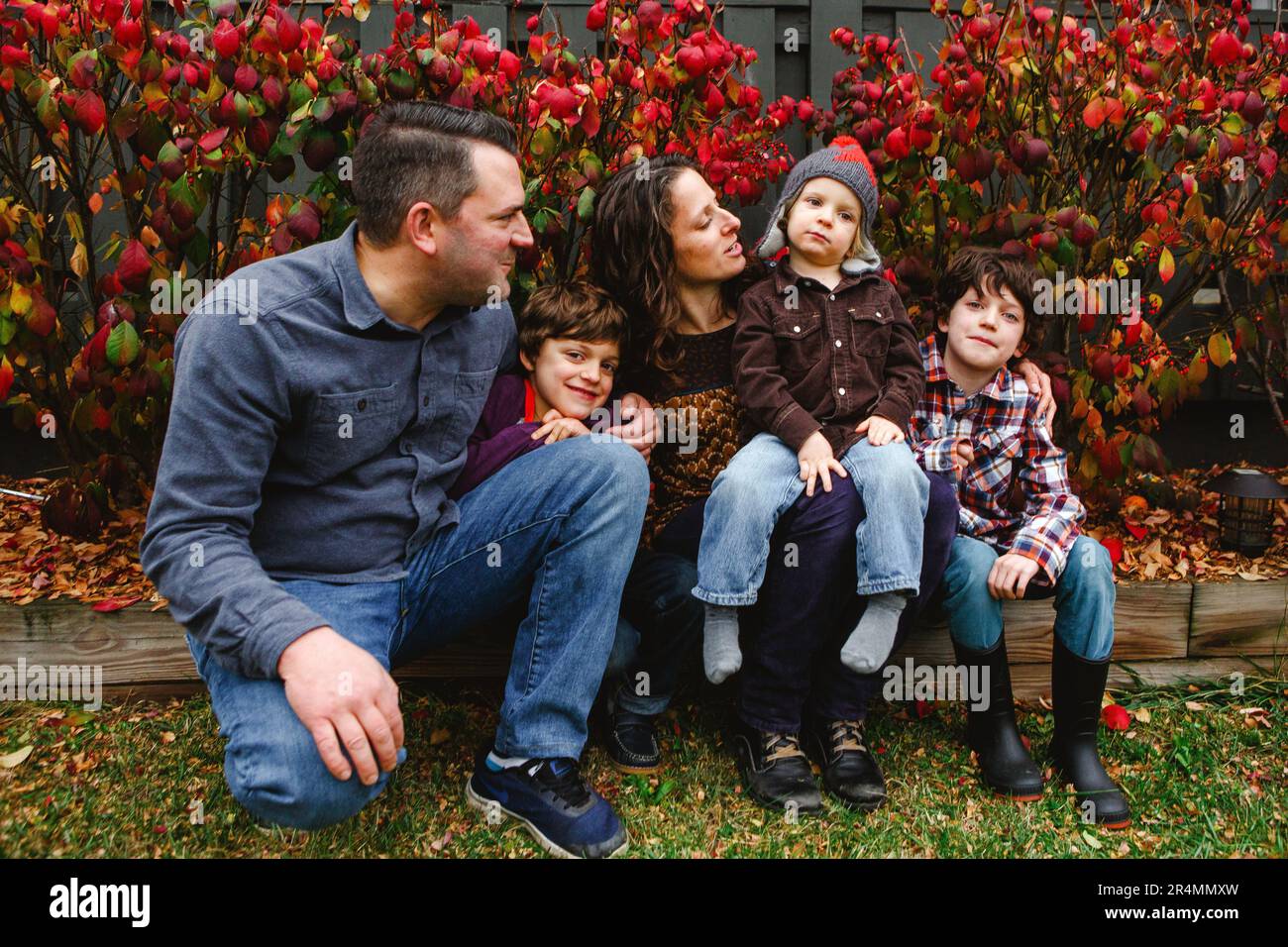 Una mamma e un papà guardano affettuosamente il piccolo figlio e si siedono con i fratelli più anziani Foto Stock